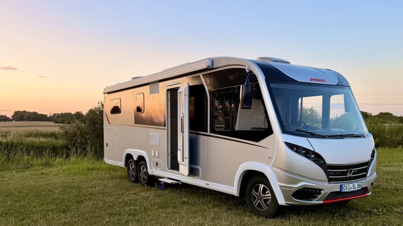 Unser Wohnmobil steht mit geöffneter Tür auf der Wiese, dahinter Felder und ein Sonnenuntergang.
