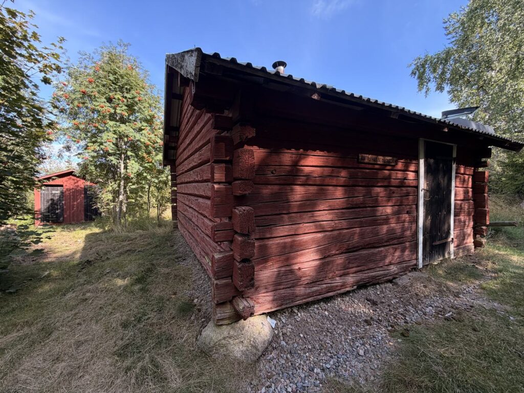 Rote Blockhütte auf einer Wiese, in der Backpacker übernachten können