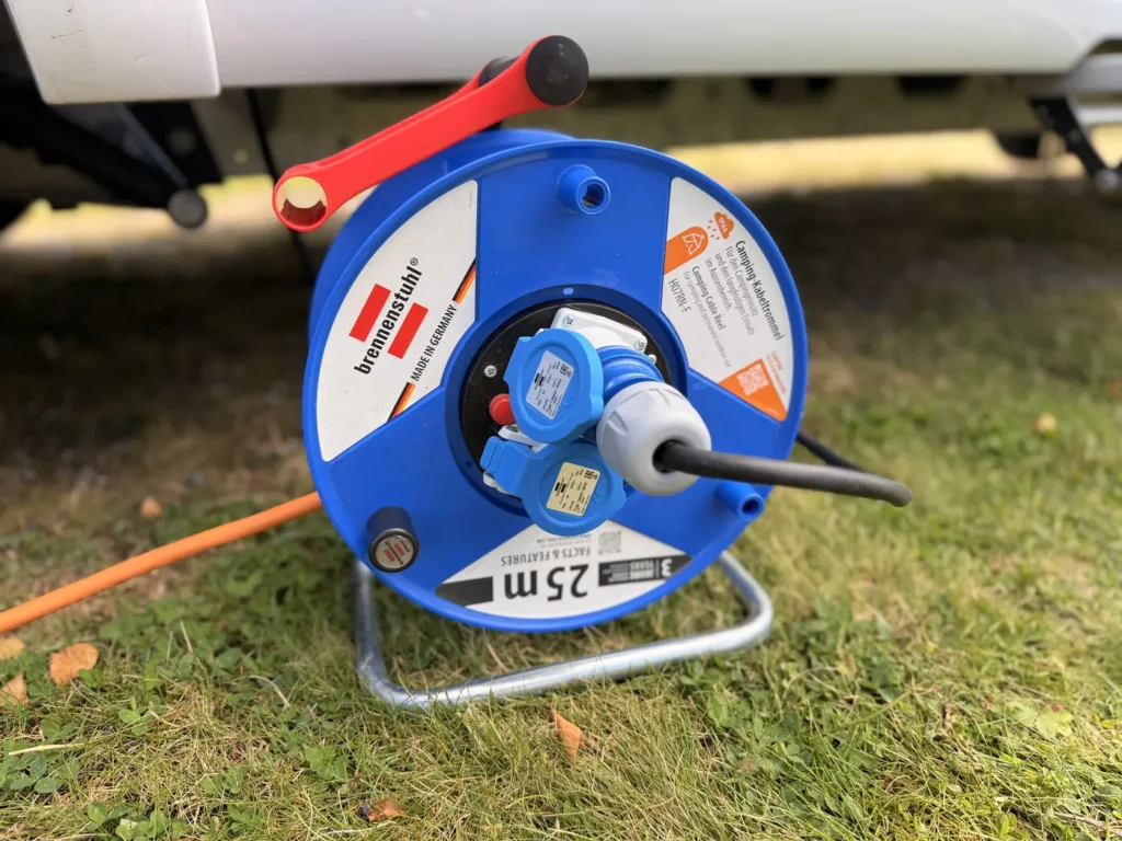 Blaue Brennenstuhl Garant Kabeltrommel mit 25 Metern Kabel steht im Gras neben dem Wohnmobil, das orange Anschlusskabel ist eingesteckt
