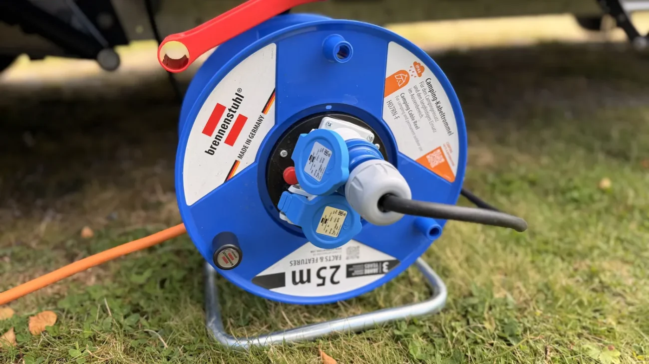 Blaue Brennenstuhl Garant Kabeltrommel mit 25 Metern Kabel steht im Gras neben dem Wohnmobil, das orange Anschlusskabel ist eingesteckt