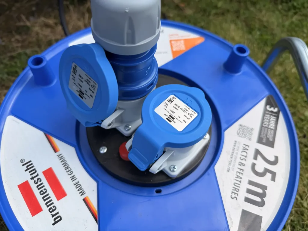 Blick von oben auf die beiden blauen Steckdosen der Kabeltrommel mit Klappdeckeln und dem roten Knopf des Überlastschutzes