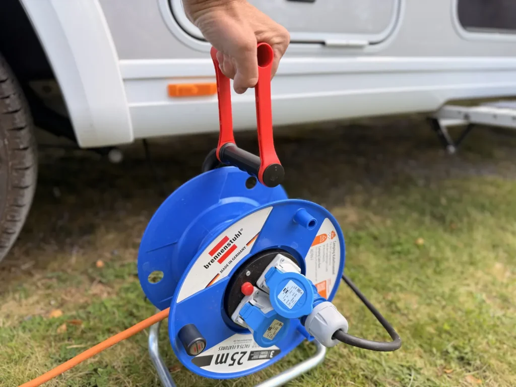 Hand hält die blaue Brennenstuhl Garant Kabeltrommel am roten Tragegriff vor dem Wohnmobil