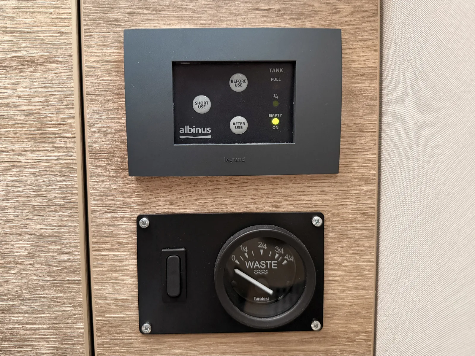 Bedienfeld der Zerhackertoilette mit den Tasten Short Use, Before Use und After Use sowie der Tankanzeige, darunter die Rundanzeige für den Abwassertank.
