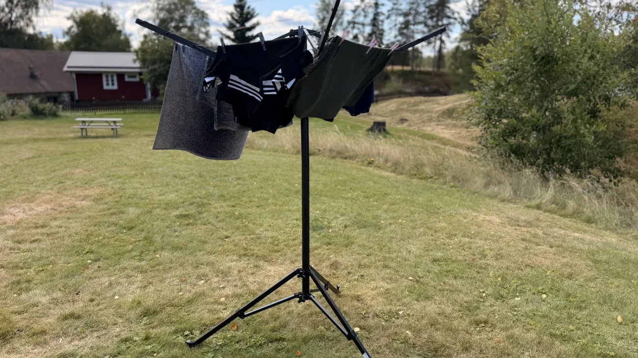 Aufgestellte Pop-up-Wäschespinne von Fritz Berger mit aufgehängter Wäsche auf einer Wiese, im Hintergrund ein rotes Holzhaus in Schweden