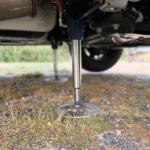 Eine ausgefahrene hydraulische Hubstütze steht mit ihrem Teller auf dem Boden unter dem Wohnmobil, dahinter ein Rad und der Unterboden.