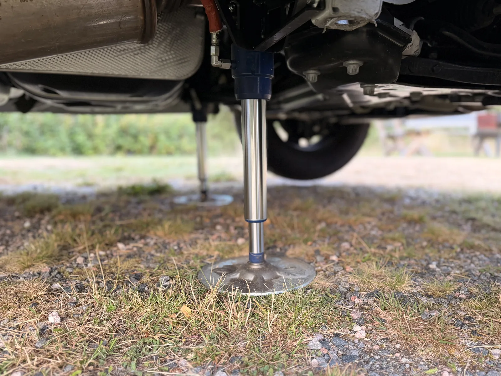 Eine ausgefahrene hydraulische Hubstütze steht mit ihrem Teller auf dem Boden unter dem Wohnmobil, dahinter ein Rad und der Unterboden.