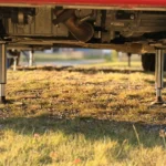 Zwei ausgefahrene Hubstützen stehen im Abendlicht auf ihren Tellern im Gras unter dem Heck des Wohnmobils.