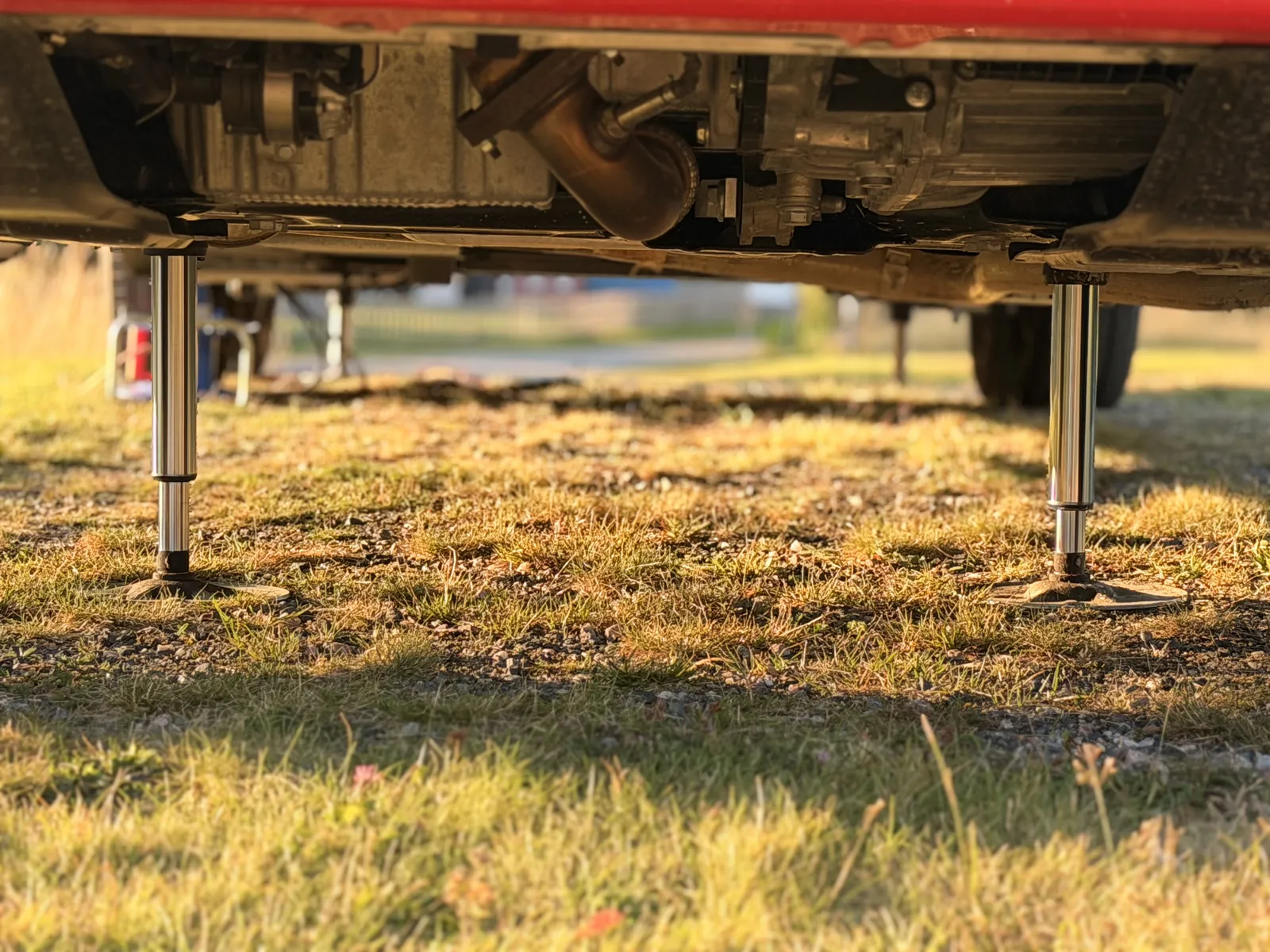Zwei ausgefahrene Hubstützen stehen im Abendlicht auf ihren Tellern im Gras unter dem Heck des Wohnmobils.