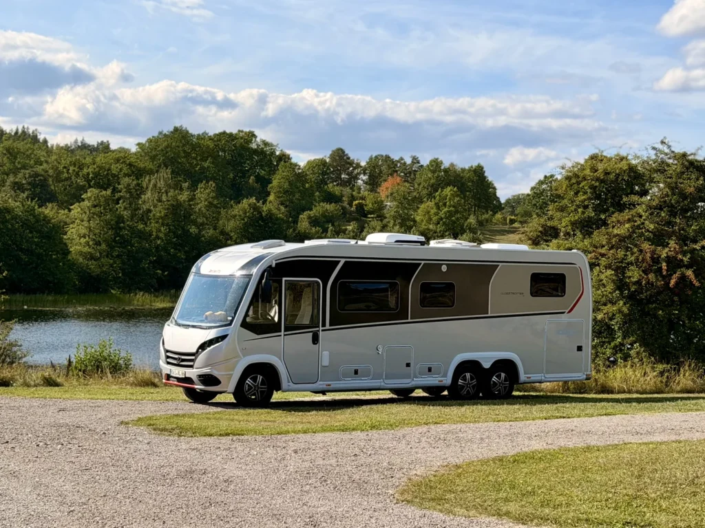 Der Dethleffs Globetrotter XLi steht auf der Wiese über dem Ufer des Sees Åsunden, im Hintergrund Wald und Wolkenhimmel.