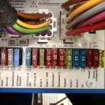 Geöffneter Sicherungskasten mit einer Reihe beschrifteter Flachsicherungen, unter anderem für Heizung, Steckdosen, Hubbett, TV und Pumpe.
