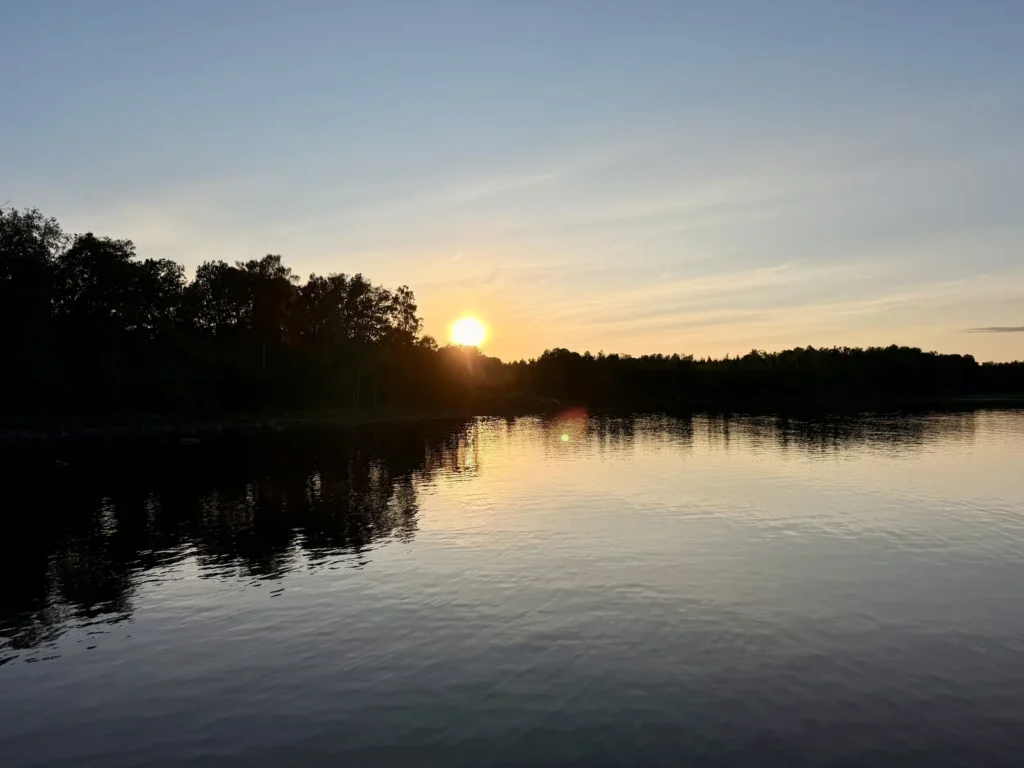 Die Sonne geht hinter der bewaldeten Uferlinie des Sees Möckeln unter und spiegelt sich in der ruhigen Wasseroberfläche.