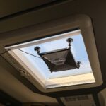 Starlink Mini hängt mit einer Saugnapfhalterung im geöffneten Dachfenster des Wohnmobils