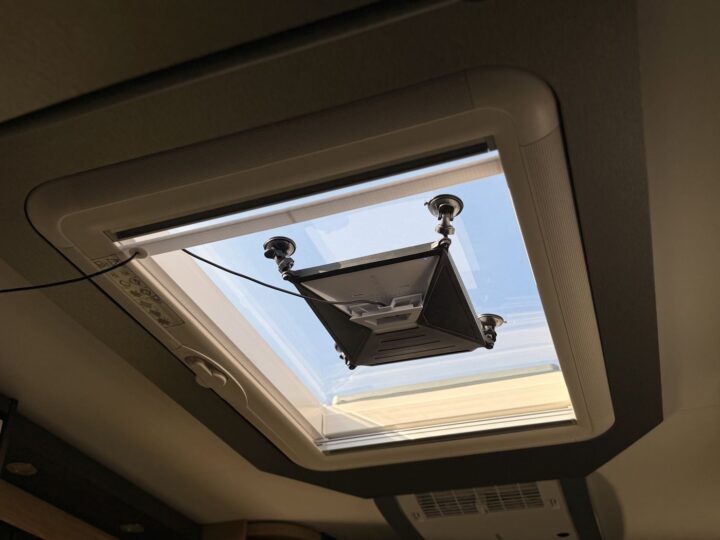 Starlink Mini hängt mit einer Saugnapfhalterung im geöffneten Dachfenster des Wohnmobils