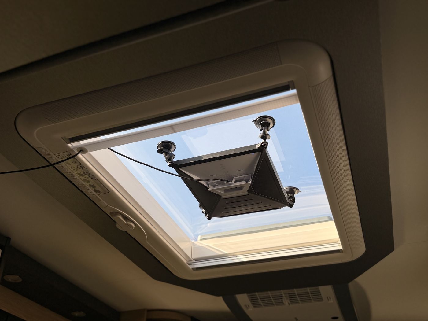 Starlink Mini hängt mit einer Saugnapfhalterung im geöffneten Dachfenster des Wohnmobils