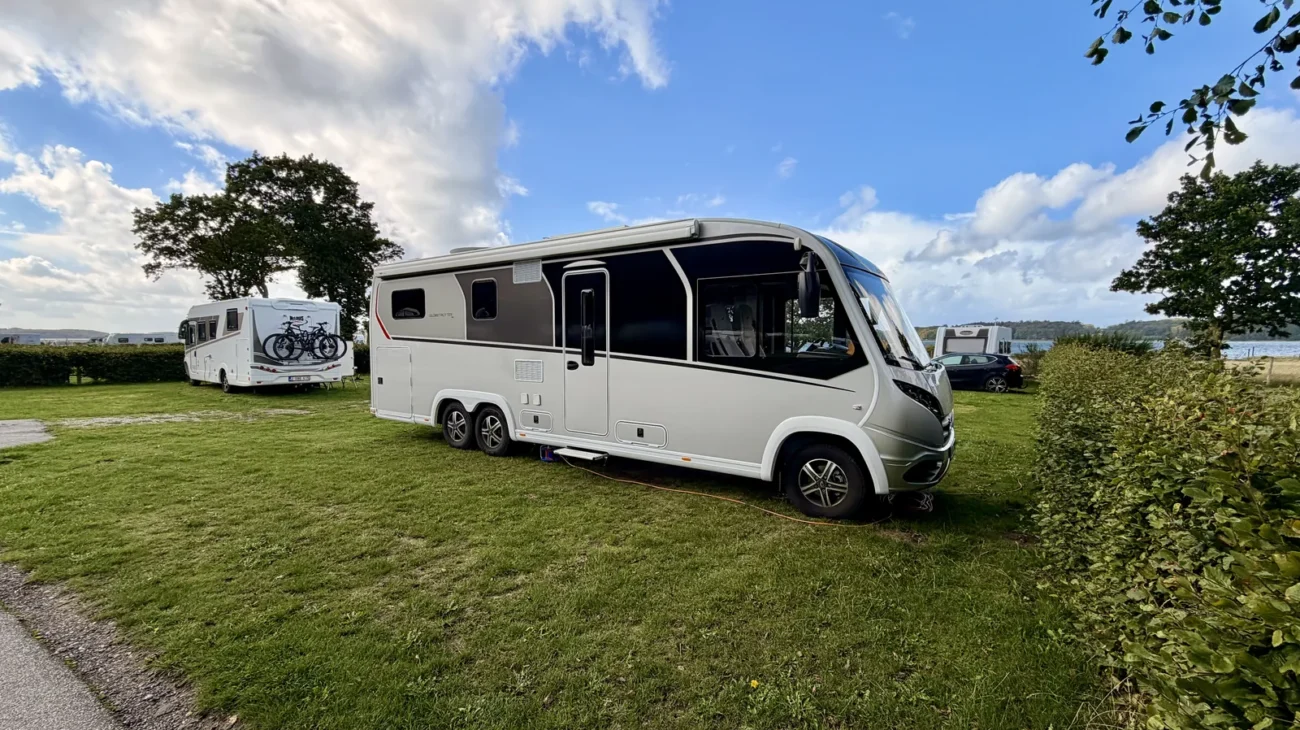 Luna steht auf der Wiese unter blauem Himmel mit Quellwolken, links ein weiteres Wohnmobil, im Hintergrund das Wasser des Lillebælt.