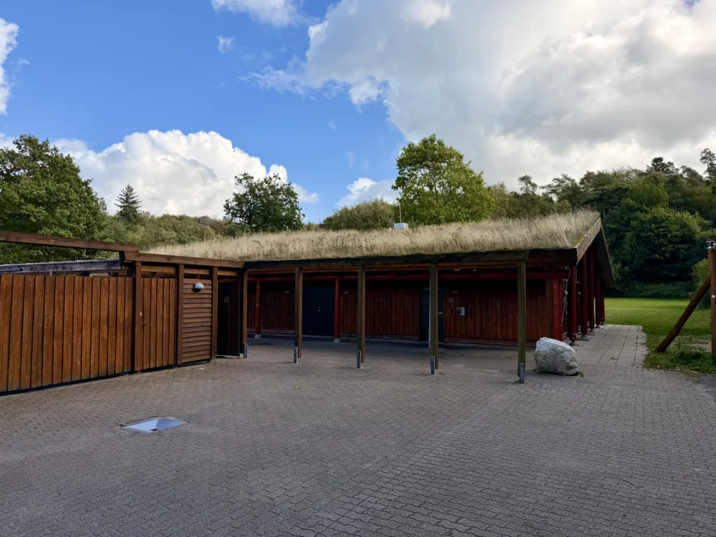 Das hölzerne Servicegebäude von Galsklint Camping mit begrüntem Grasdach und überdachtem Vorbereich auf gepflastertem Platz.