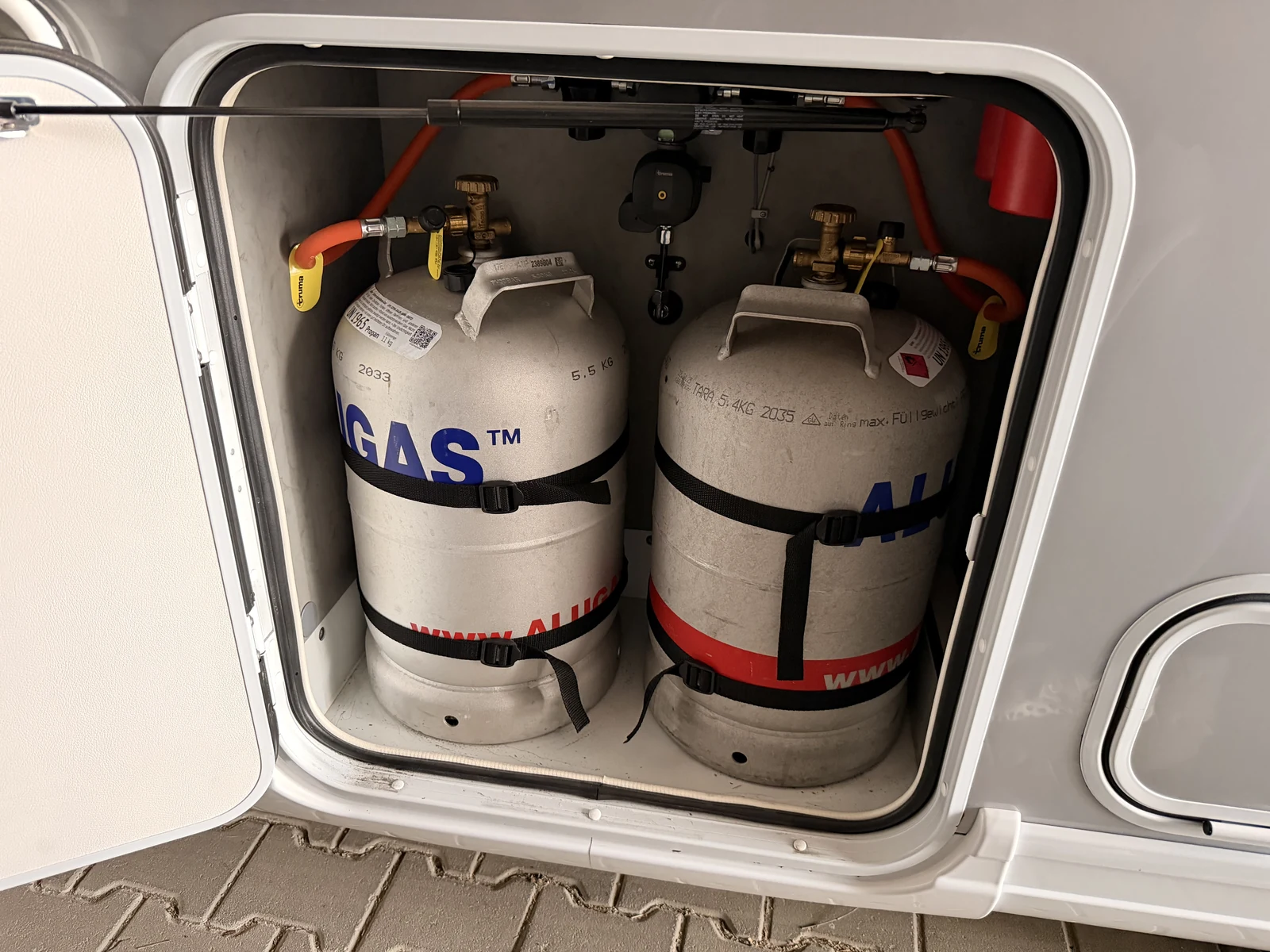 Geöffneter Gaskasten des Wohnmobils mit zwei angegurteten Alugas-Flaschen, roten Gasschläuchen und der Umschaltautomatik darüber