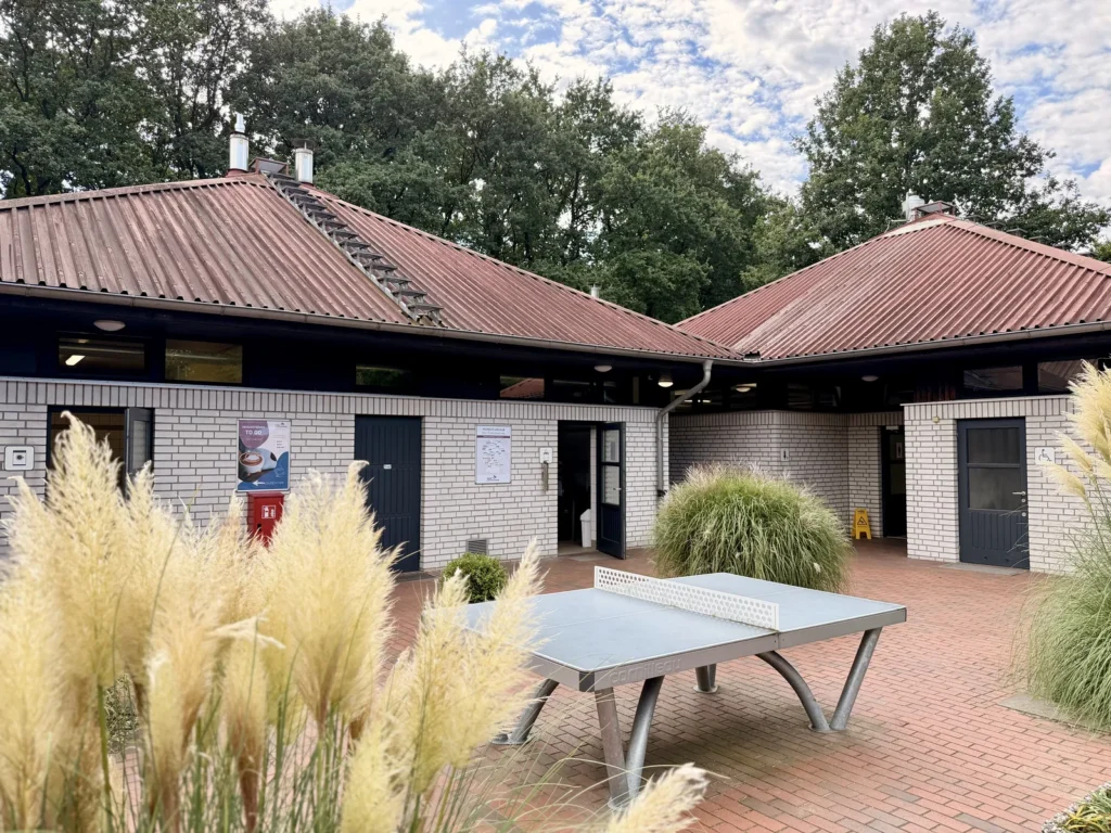 Sanitärgebäude aus hellem Klinker mit rotem Dach, davor ein gepflasterter Innenhof mit Tischtennisplatte.