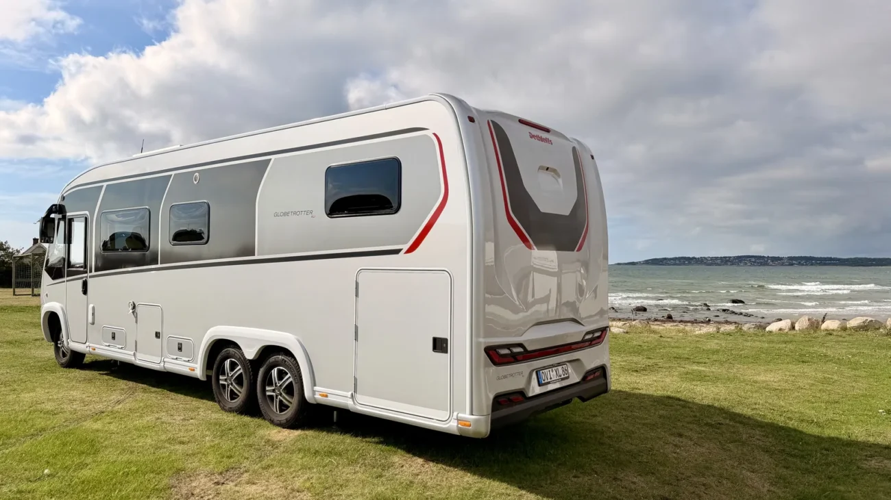 Der Dethleffs Globetrotter XLi steht schräg von hinten auf der Wiese von Platz SX3, rechts dahinter die Brandung und das Steinufer, links ein Fußballtor.