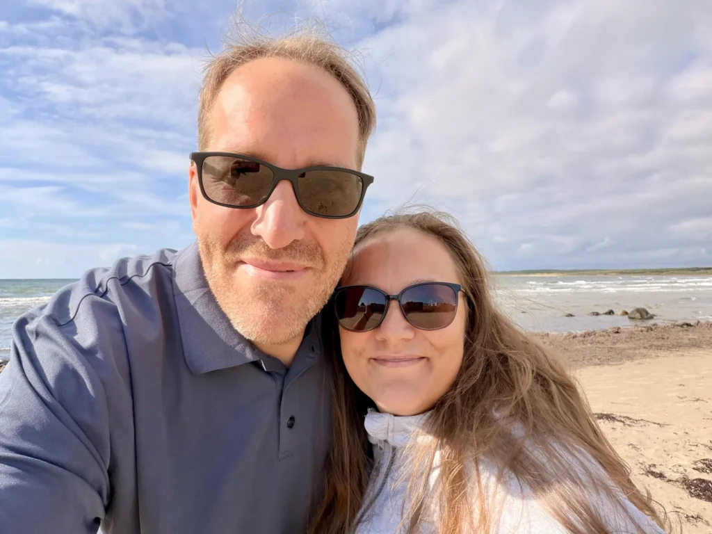 Michael und Maria mit Sonnenbrillen am Strand, hinter ihnen die Brandung und der weite Sandstrand.
