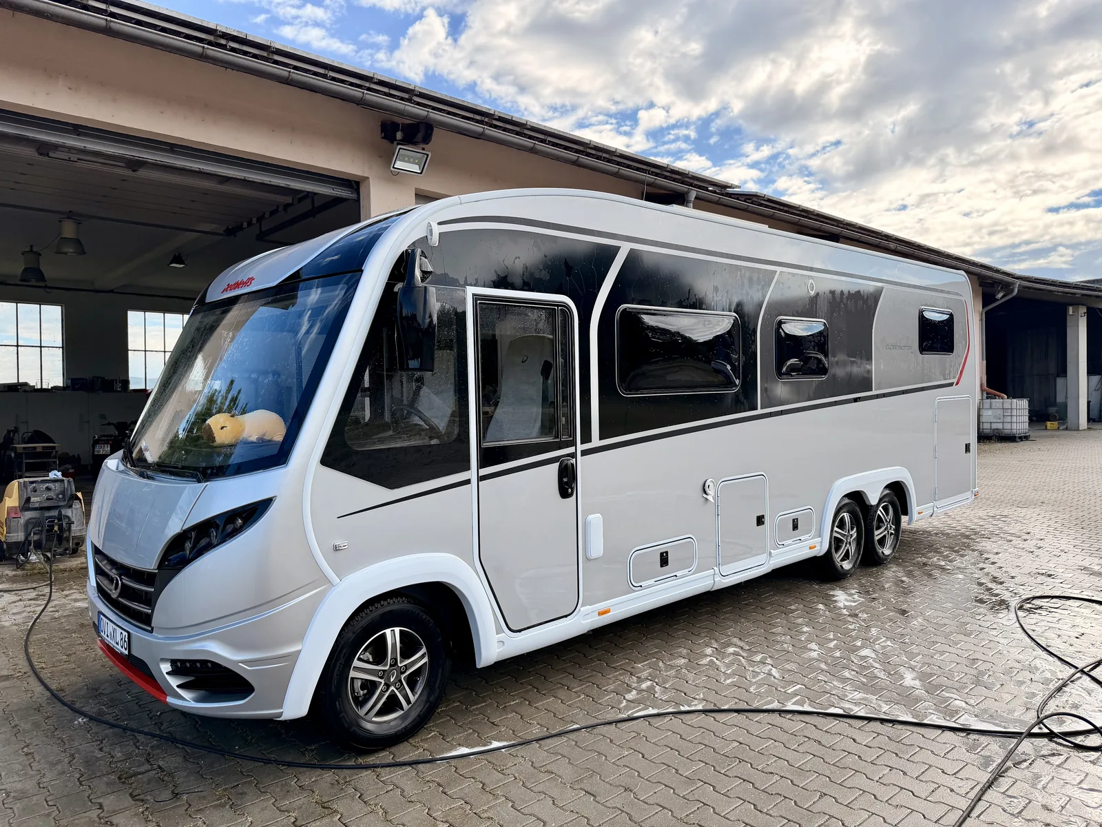 Das frisch abgespülte, noch nasse Wohnmobil steht vor der Halle, Lack und Fenster sind sauber.