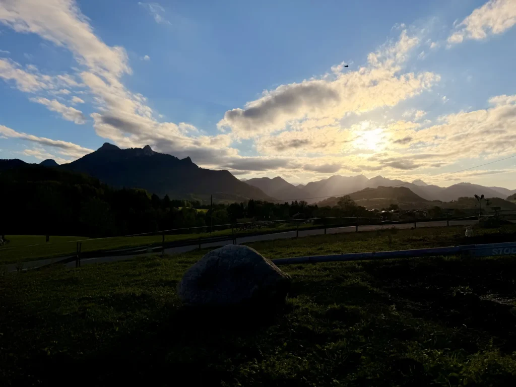 Abendsonne über den Bergen am Samerberg, im Vordergrund eine Wiese mit einem großen Stein