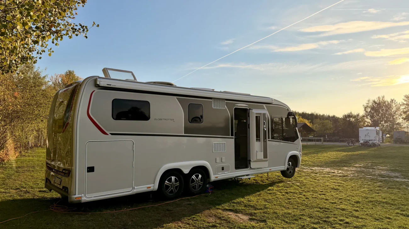 Unser Dethleffs Globetrotter XLi Luna mit offener Aufbautür auf der Wiese des Wohnmobilstellplatzes am Steinberger See, die Hubstützen sind ausgefahren, im Hintergrund tief stehende Abendsonne und weitere Wohnmobile